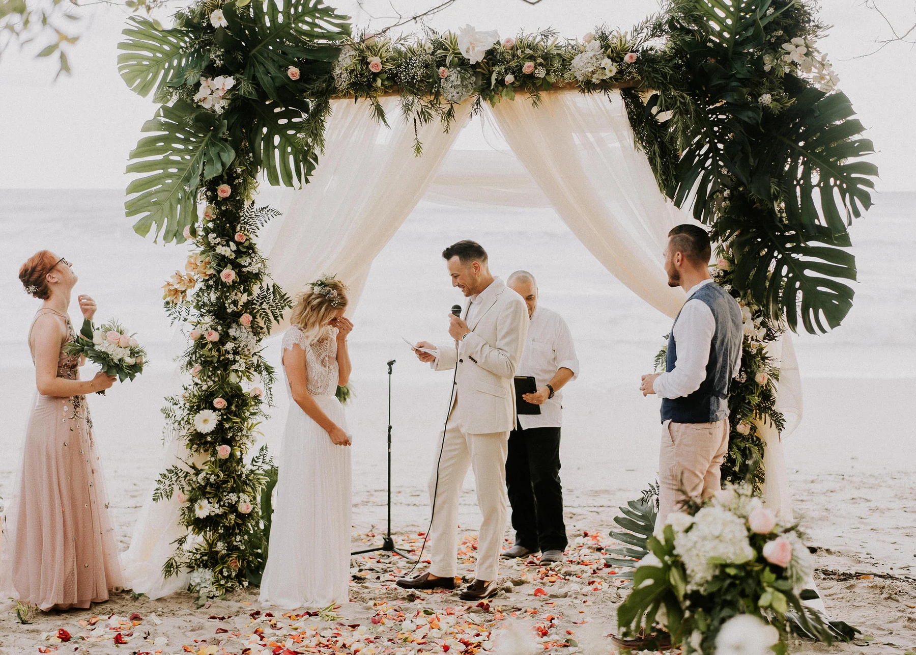 Wedding ceremony beneath a flower-covered beach arch